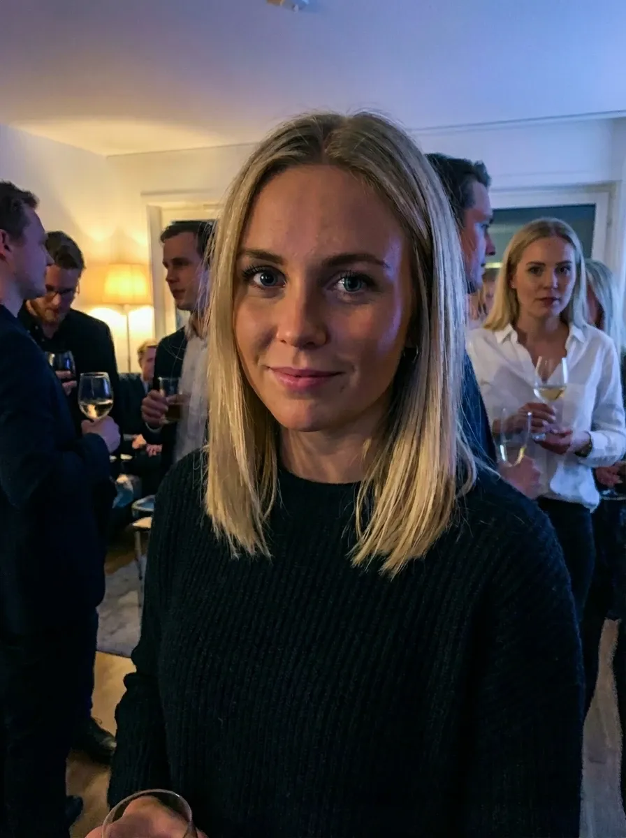 Indoor party photo of a blonde woman in a black sweater holding a drink